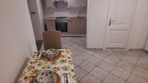 Ein Essbereich mit Tisch für vier Personen, eine Küche im Hintergrund und eine geschlossene Tür.