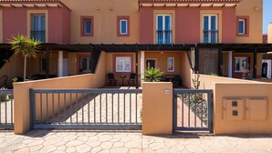 Una hilera de casas urbanas de color terracota con balcones, una entrada porticada y un patio empedrado.