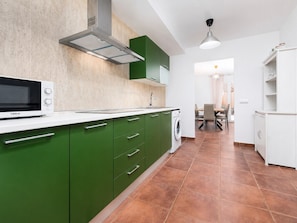 Una cucina moderna con mobili verdi, un piano di lavoro bianco, un forno a microonde e una lavatrice.