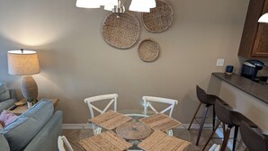 A dining area with a round glass table, white chairs, and woven placemats. - Beach Beau (Long Beach)
