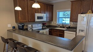 A kitchen with wooden cabinets, a granite countertop, a built-in oven, a microwave, a sink, a refrigerator, and bar stools. - Beach Beau (Long Beach)
