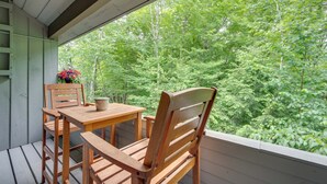 Terraza de madera con mesa y sillas, con vistas a un bosque frondoso.
