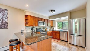 Una cocina moderna con encimeras de granito, electrodomésticos de acero inoxidable, armarios de madera y una isla grande con taburetes de bar.