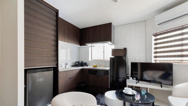 A compact kitchen with modern appliances, a dining area with a small table, and a sofa. - Hotel Kiki (Osaka)