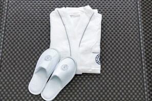 A neatly folded white robe and a pair of white slippers on a checkered surface. - Hotel Kiki (Osaka)