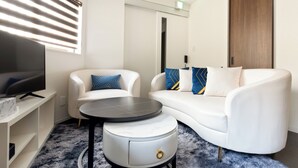 A modern living room with a white sofa, a round coffee table, and a TV on a stand. - Hotel Kiki (Osaka)