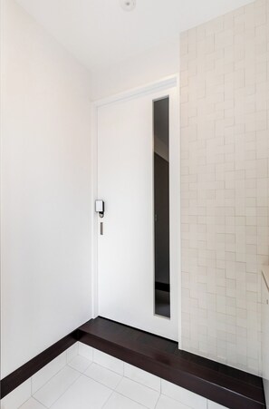 A hallway with a white door, a dark brown bench, and a tiled wall with a geometric pattern. - Hotel Kiki (Osaka)