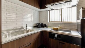 A modern kitchen with white subway tiles, wooden cabinets, a stainless steel sink, and a window above the counter. - Hotel Kiki (Osaka)
