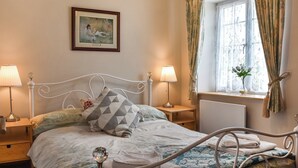 A bedroom with a bed, two bedside lamps, a window with curtains, a bedside table, and a framed picture on the wall. - Curlew Cottage - UK47697 (Haydon Bridge)
