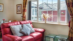 A red leather sofa with grey cushions, a glass coffee table, and a window with a view of a red fence and a house. - Curlew Cottage - UK47697 (Haydon Bridge)