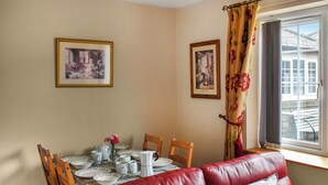 A dining area with a table set for four, a red leather sofa, and two framed pictures on the wall. - Curlew Cottage - UK47697 (Haydon Bridge)
