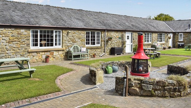 A stone building with a tiled roof, a bench, a red lantern, and a grassy courtyard. - Curlew Cottage - UK47697 (Haydon Bridge)