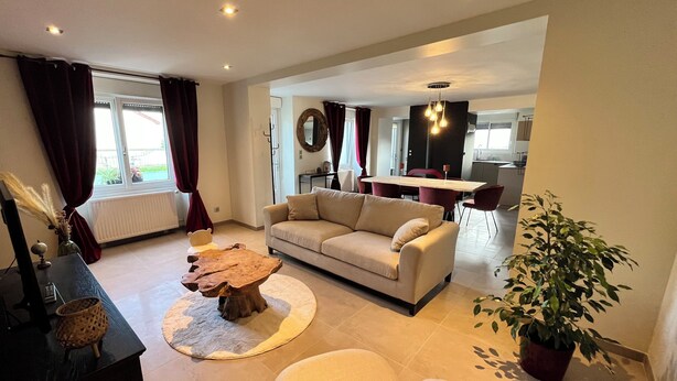 A modern living room with a sofa, a coffee table, and a dining area in the background. - Gîte La Rosalie (La Forestière)