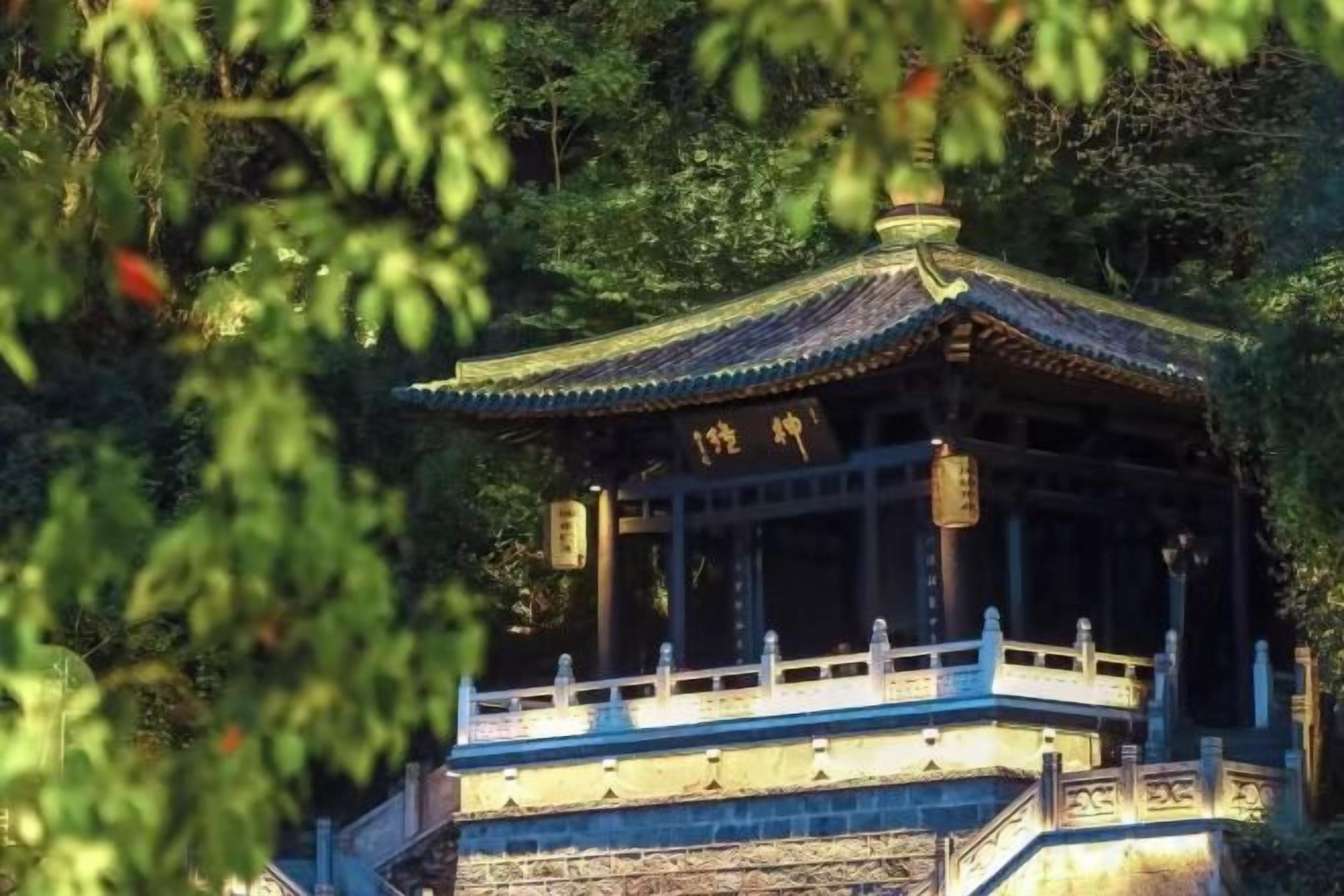 A traditional pavilion with a tiled roof, surrounded by trees.