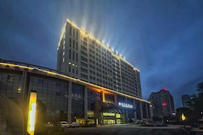 A multi-story hotel with a prominent entrance and a large building in the background.