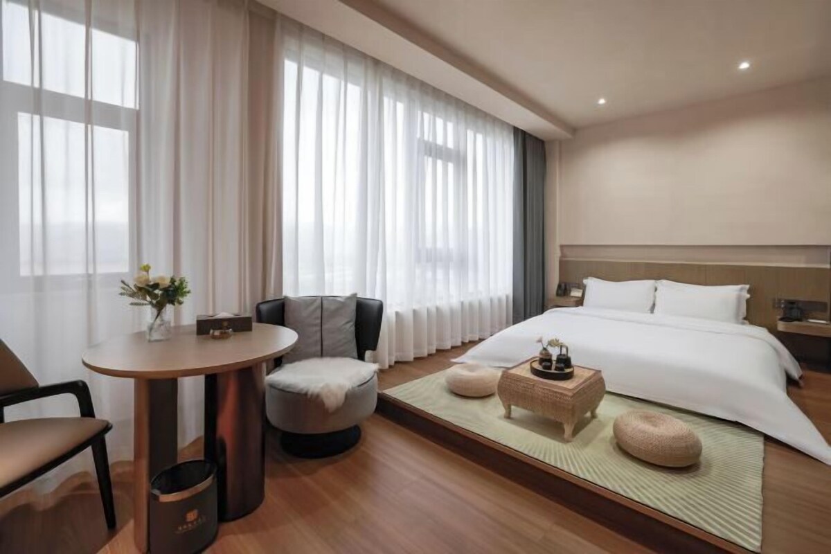 Une chambre d’hôtel moderne avec un grand lit, une table ronde, un canapé et une petite table sur laquelle est posé un vase de fleurs.