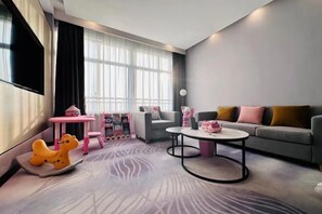 A modern living room with a grey sofa, a coffee table, a rocking horse, and a pink play table.