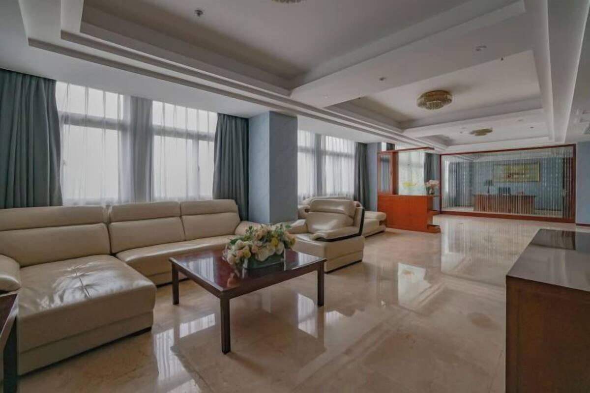 Un salón espacioso con un sofá color beige, una mesa de centro con flores y un ventanal con cortinas.