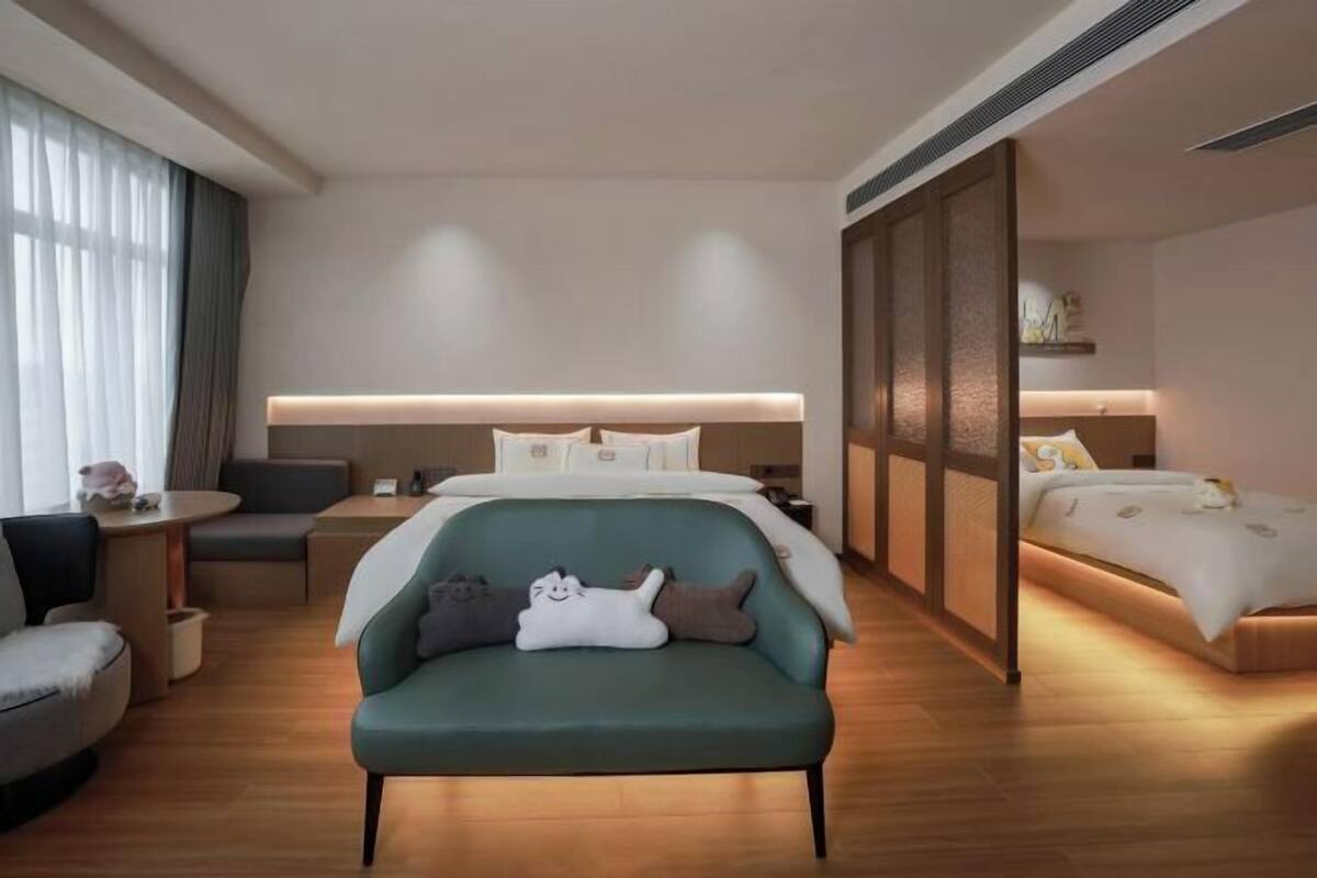 Una habitación de hotel moderna con sofá, cama, escritorio y un amplio ventanal con cortinas.