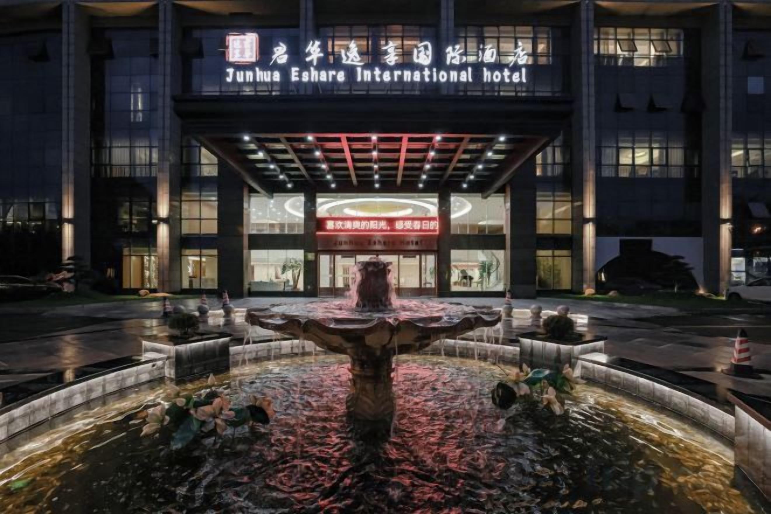 A hotel entrance with a fountain in the foreground and a sign for Junhua Eshare International Hotel.