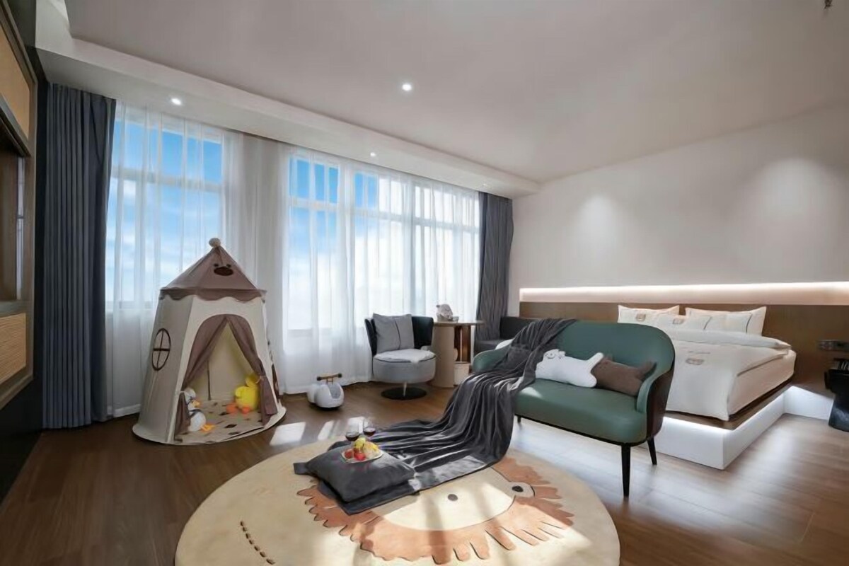 Une chambre d’hôtel moderne, dotée d’une tente de jeu accueillante, d’un canapé confortable, d’un tapis rond et d’un lit soigneusement fait.