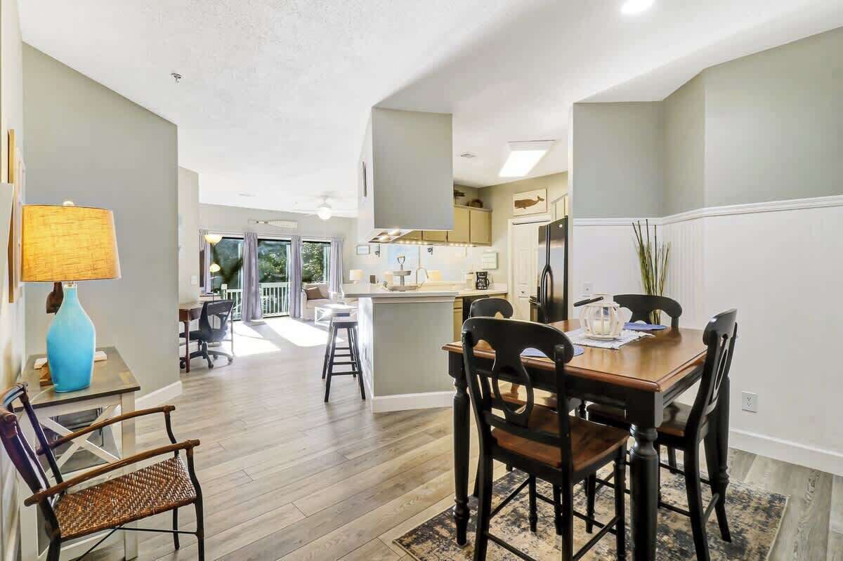 A spacious kitchen with a central island, a dining area with a wooden table and chairs, and a view of the outdoors through large windows.
