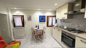 A compact kitchen with a gas stove, sink, and a dining table set for two. - Cupido Suite by Ca-sa Check (Venice)