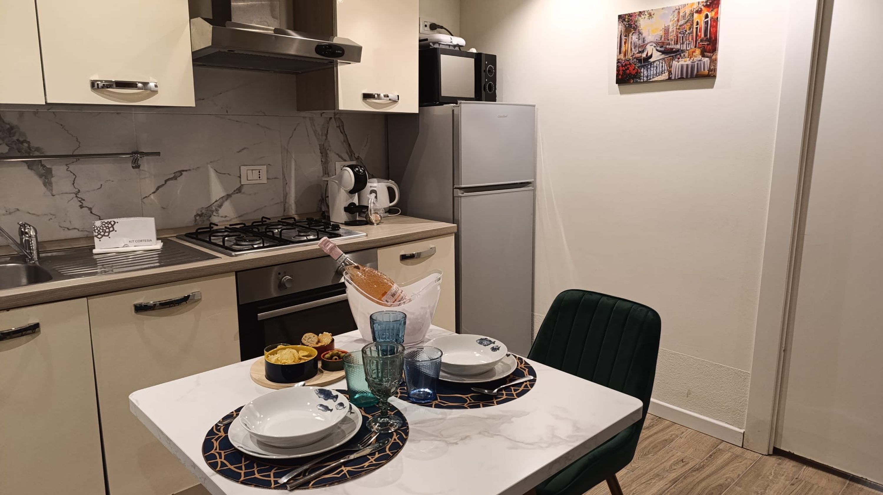A compact kitchen with a gas stove, microwave, and refrigerator. A dining table with plates and cutlery is set.