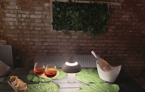 A table with two glasses of red wine, a bottle of champagne, and a white bowl with a green leaf-patterned placemat.