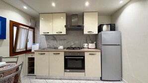 A compact kitchen with a gas stove, oven, and a built-in microwave. There is a refrigerator and a window with curtains. - Cupido Suite by Ca-sa Check (Venice)