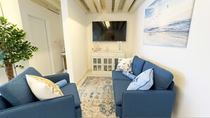 Ein Wohnzimmer mit zwei blauen Sofas, einem großen Flachbildfernseher, einer Vitrine und einem Bild an der Wand.