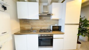 Eine kleine Küche mit weißen Schränken, einem Gasherd, einer Mikrowelle und einem Backofen.