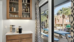 Una habitación con un armario de madera, una cafetera y vistas a un patio exterior con mesas y palmeras.