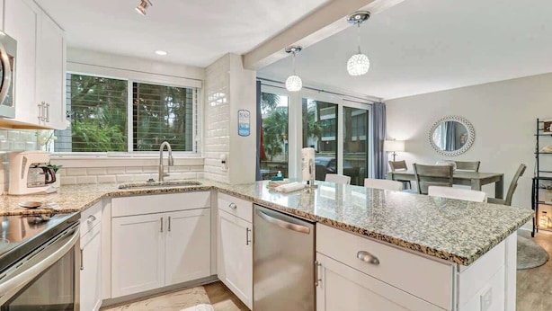 A modern kitchen with white cabinetry, granite countertops, stainless steel appliances, and a large window providing natural light.