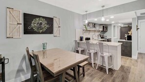 Una cocina moderna con armarios blancos, una mesa de comedor de madera y una lámpara colgante.