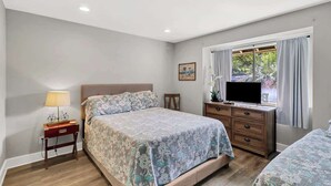 Un dormitorio con cama, mesita de noche con lámpara, cómoda y ventana con cortinas.