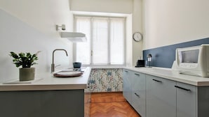 Une cuisine moderne avec un parquet en bois disposé en chevrons, un four à micro-ondes encastré et une fenêtre avec des stores.