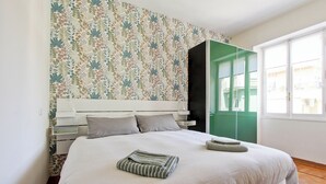 Un lit bien fait, avec une couverture à rayures, une tête de lit blanche et un papier peint à motifs floraux.