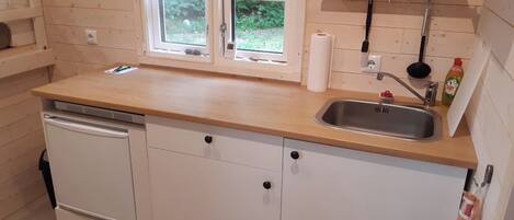 A compact kitchen with a wooden countertop, a built-in dishwasher, a sink, and a window with a view of greenery.
