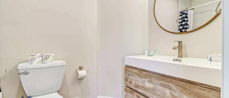 Un baño con inodoro, lavamanos con tocador de madera, espejo y toallero.