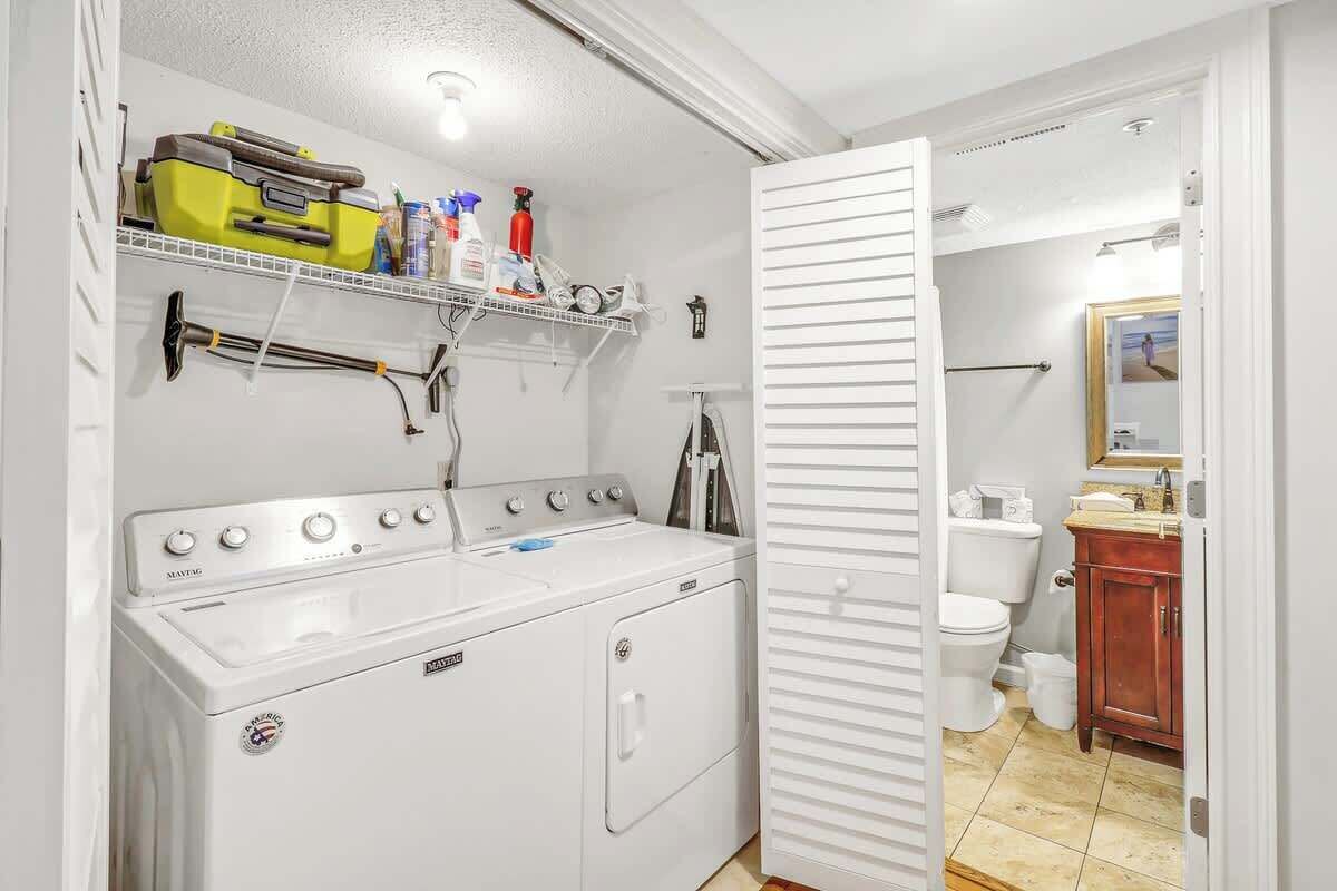 Un área de lavandería con lavadora y secadora, un estante con productos de limpieza y un baño con inodoro y lavamanos.