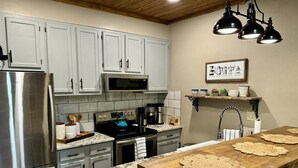 A modern kitchen with white cabinets, stainless steel appliances, a wooden island with placemats, and a coffee station. - Ski-In/Ski-Out • Romantic Studio • Near Trails (Angel Fire)