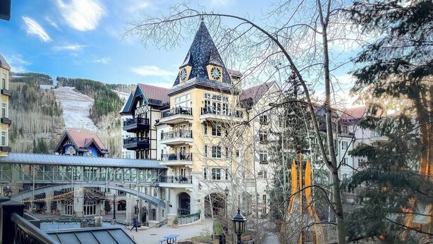 A hotel with a prominent tower, a covered walkway, and a ski slope in the background. - Lover's Landing | Walk to Gondola | Rooftop Hot Tub #026194 (Vail)