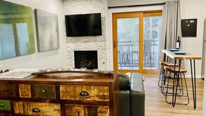 A modern living room with a fireplace, a television mounted on the wall, a dining area with a table and chairs, and a balcony with outdoor furniture. - Lover's Landing | Walk to Gondola | Rooftop Hot Tub #026194 (Vail)