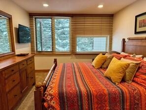 Een slaapkamer met een groot bed, een houten dressoir en een televisie aan de muur.