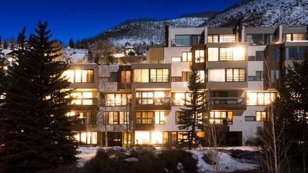 Un hôtel à plusieurs étages, avec des fenêtres illuminées, entouré d’arbres couverts de neige et avec une montagne en arrière-plan.