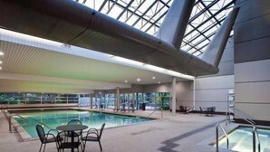 Une piscine intérieure dotée d’un toit en verre, une table avec des chaises et un espace aménagé au bord de la piscine.