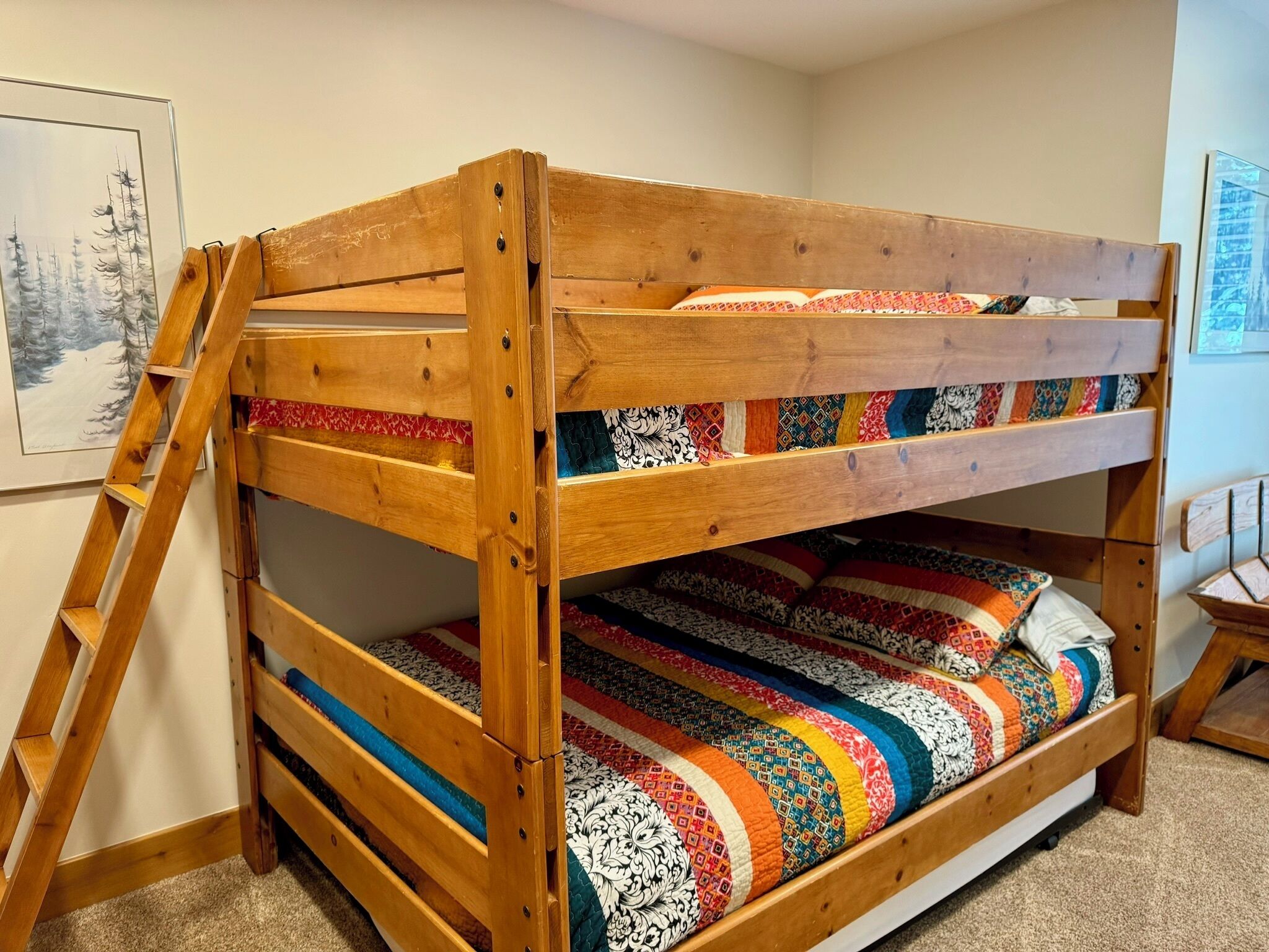 A bunk bed with a ladder, colorful quilts, and a framed picture on the wall.