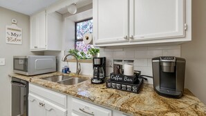 A kitchen with white cabinets, a granite countertop, a coffee maker, a microwave, and a coffee bar sign.