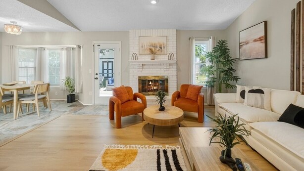 A living room with a fireplace, two armchairs, a sofa, a coffee table, and a dining area with a table and chairs.